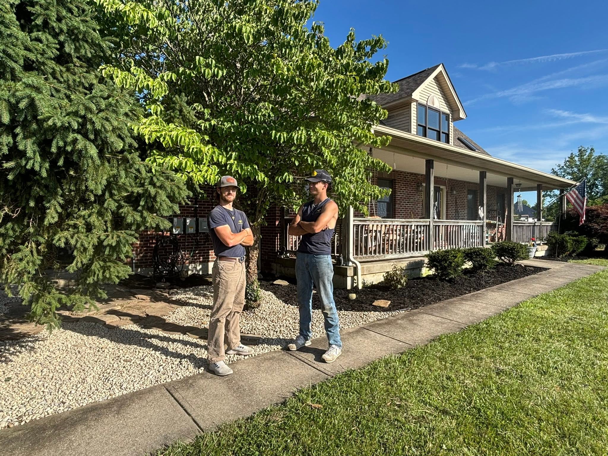 Two team members standing on a gravel landscape bed beside a lawn in front of a home with a covered porch