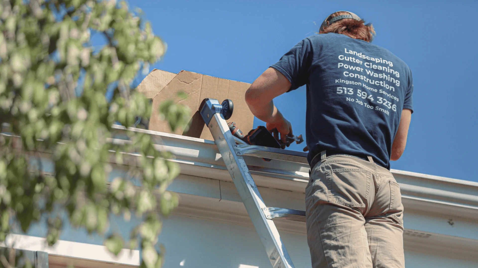 Kingston Home Services worker on an aluminum ladder at a home gutter line under a clear blue sky