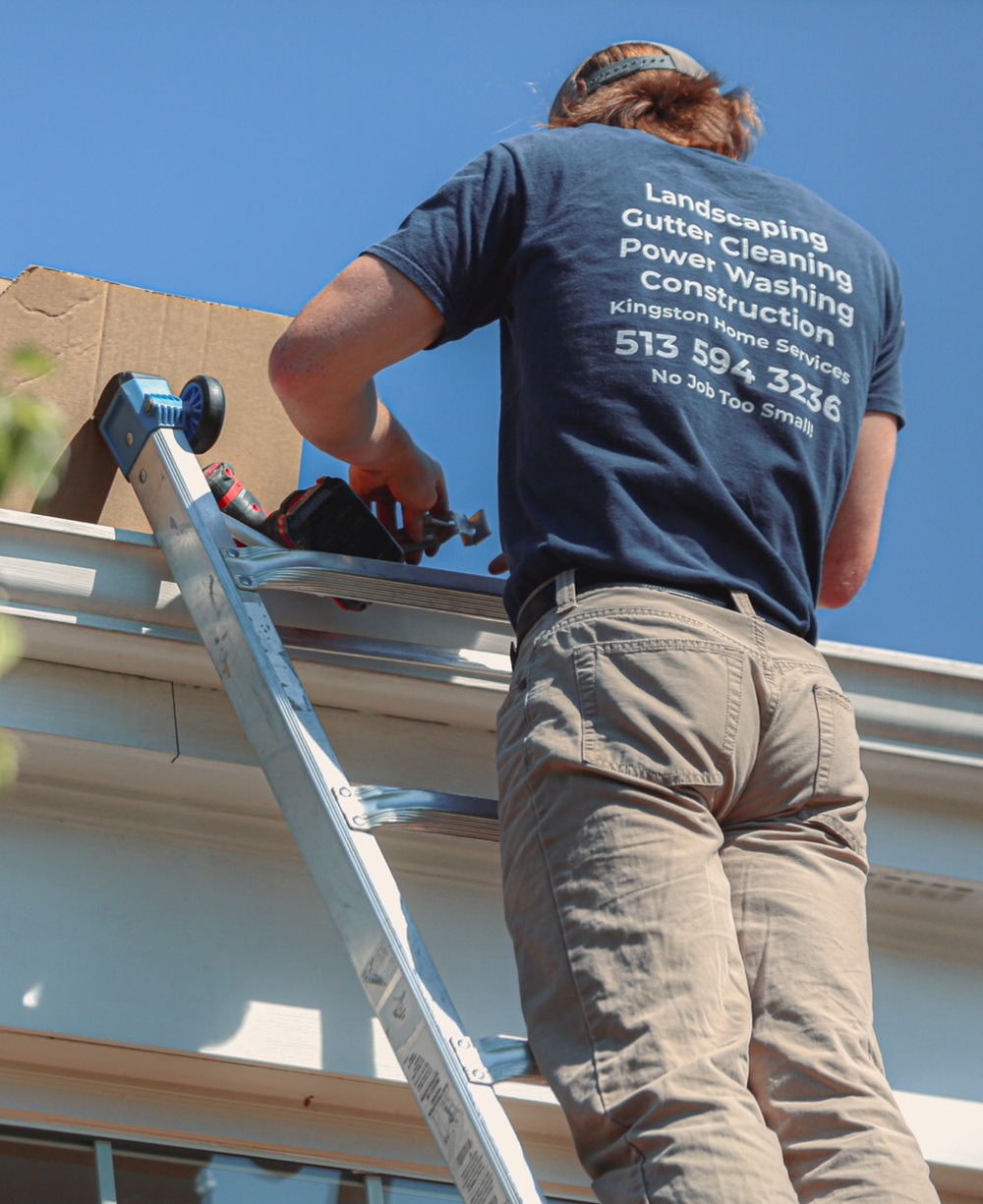 Worker in a Kingston Home Services shirt on a ladder repairing a white gutter and fascia board